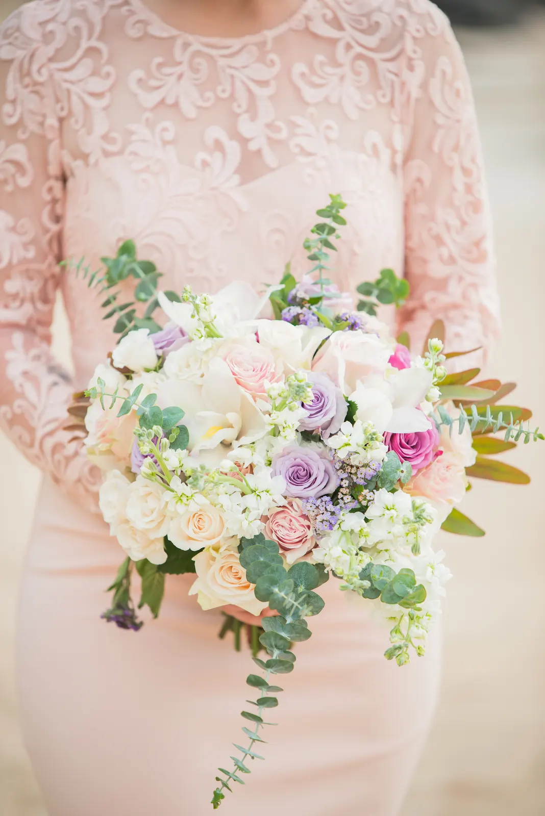 A bride holding a loose bouquet of cream and blush roses with eucalyptus