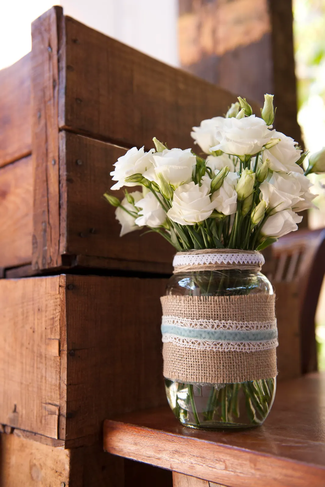 White lisianthus in a lace-wrapped jar on a wooden ledge