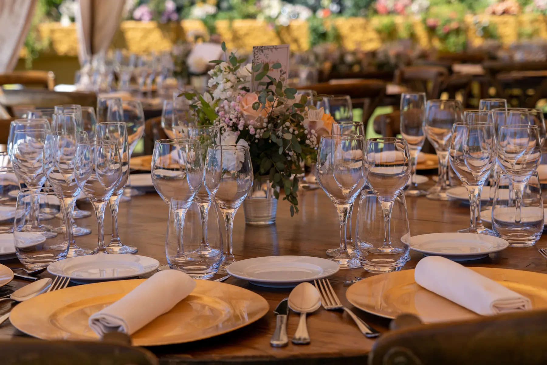 A round table set with glassware, gold chargers and a low centerpiece of garden flowers